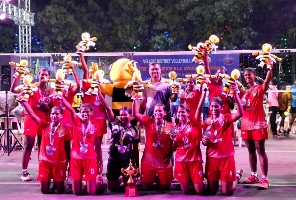 Women's volleyball team in red celebrating with medals, trophies and mascots after winning a tournament.