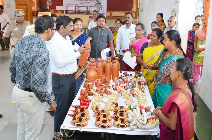 Women browsing and buying jewelry and handicrafts at a colorful bazaar inside a hall, with various stalls displaying ornaments, accessories, and handmade items.