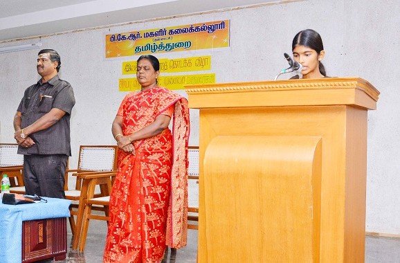 A student delivers a speech at the podium during the inauguration of the Tamil Literary Association at PKR Arts College for Women, with faculty members standing on the stage behind her.