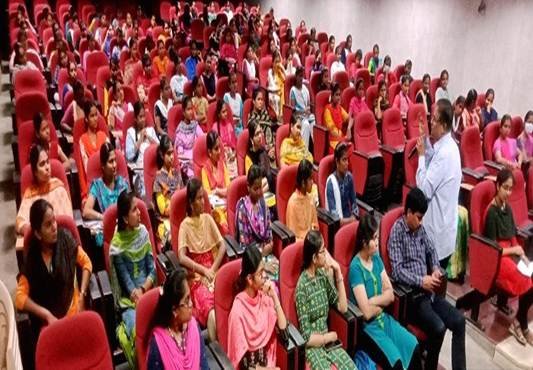 Students attending a seminar at PKR Arts College, with a faculty member addressing the audience in a packed auditorium.