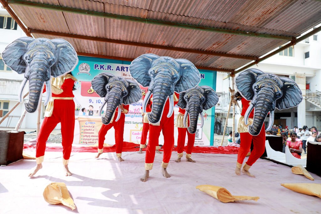 Students perform a creative stage dance wearing red costumes and large elephant head props during a cultural event at P.K.R. Arts College for Women.